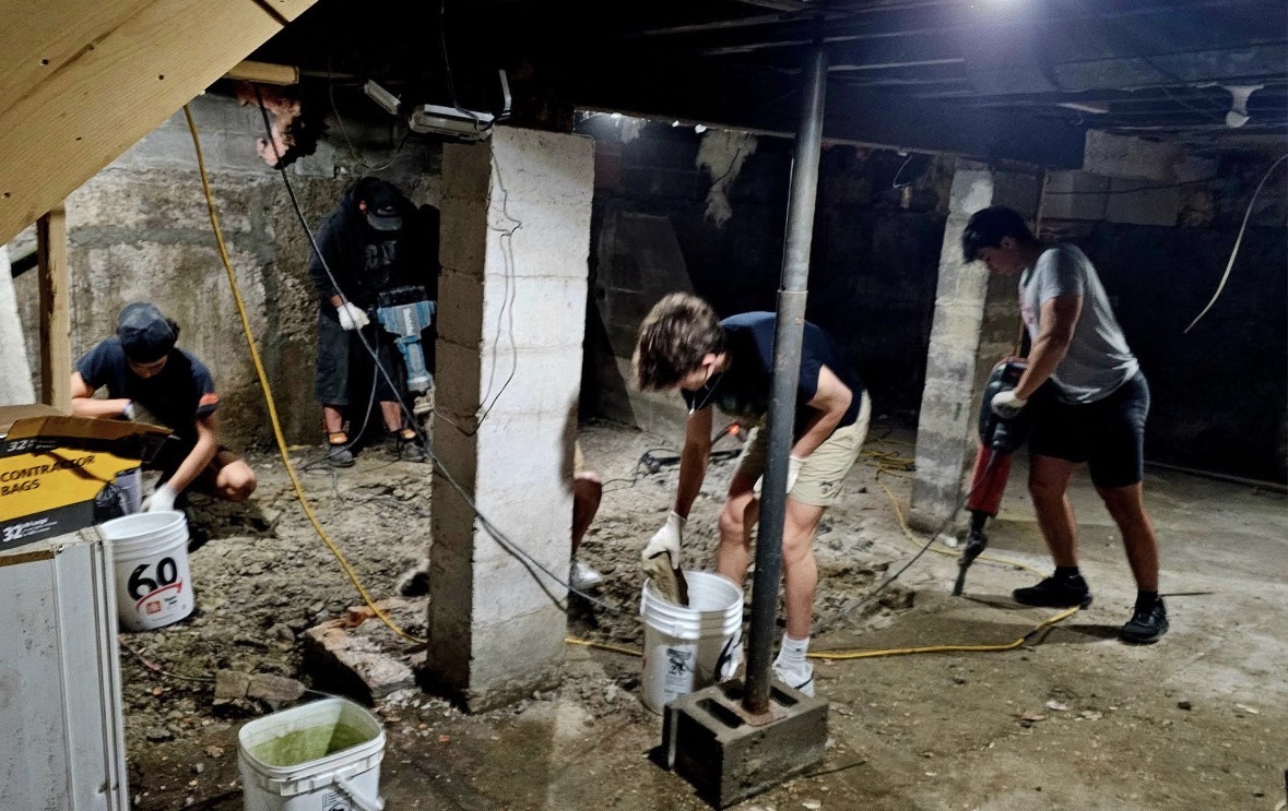 Crew breaking up basement concrete with jackhammers and buckets.